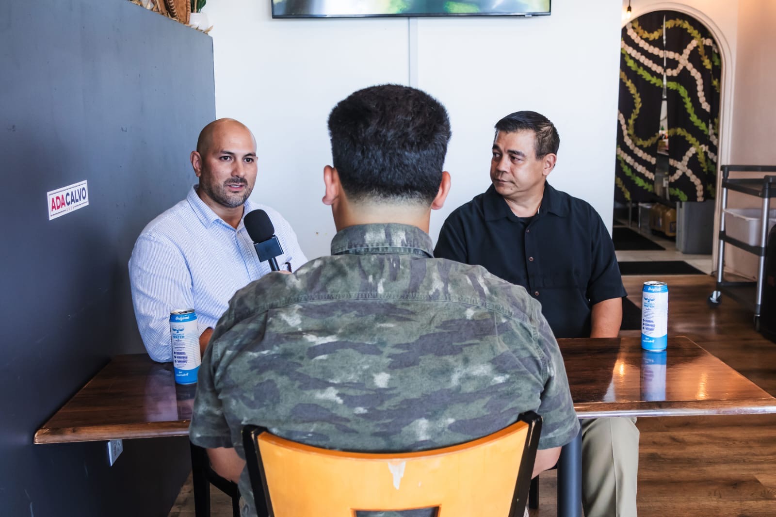 Genesis Babauta interviews Tony Ada and EJ Calvo over lunch with the Ada Calvo sign behind them